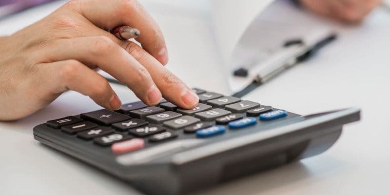 Mão segurando uma calculadora com recibos de impostos ao lado.